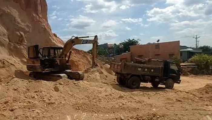 Bên dưới quả đồi, xe múc liên tục múc đất lên xe ben