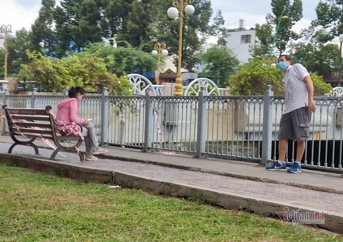 Ghế ngồi công cộng dọc bờ kênh, lực lượng chức năng quấn dây để cấm nhưng một phụ nữ vẫn ngồi đè lên