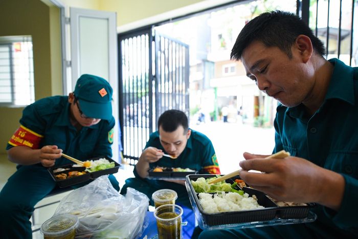  Tranh thủ ăn cơm trong thời gian nghỉ ngắn ngủi giữa trưa hè nắng nóng, anh Đỗ Thành Đô (phải), Đội trưởng đội dân quân phường Vĩnh Phúc, chia sẻ: "Nắng nóng, anh em ai cũng mệt. Thật may có những suất cơm ngon, canh ngọt mọi người đem tặng. Chúng tôi ai cũng ăn hết". 