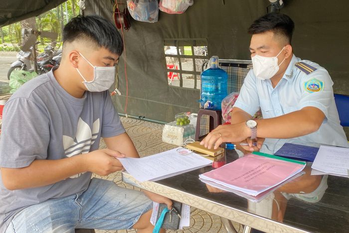 Nam thanh niên cầm phiếu đi chợ đã hết hạn ra đường và bị lập biên bản. Ảnh: An Huy.