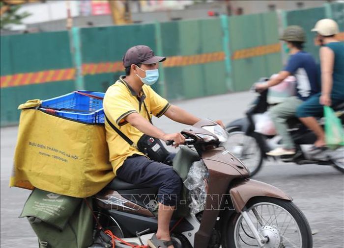 Nhân viên giao hàng đội mũ vải thay cho mũ bảo hiểm khi di chuyển trên phố (ảnh chụp sáng 10/8/2021).