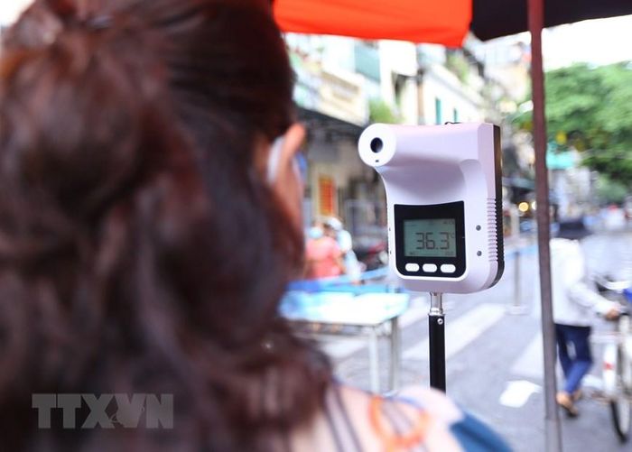 Người vào khu vực chợ Hàng Bè đều được kiểm tra thân nhiệt. (Ảnh: Hoàng Hiếu/TTXVN)