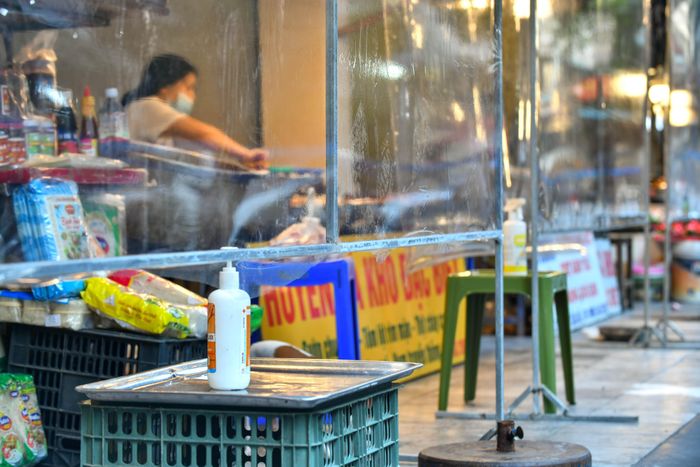  Phía dưới tấm chắn là bàn đặt thực phẩm, cùng với gel rửa tay khô. Khách hàng và tiểu thương trao đổi, mua bán qua bàn đặt, hạn chế tiếp xúc trực tiếp. 