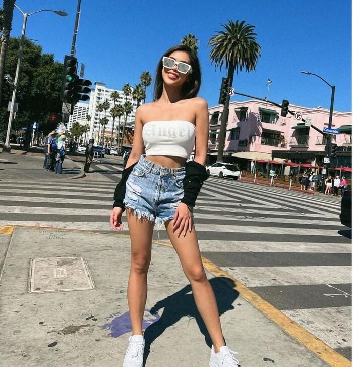Cô nàng mặc áo quây trắng mix cùng quần jeans ngắn cạp cao bụi bặm đi kèm giày thể thao và áo cardigan croptop đen khoác hờ bên ngoài 
