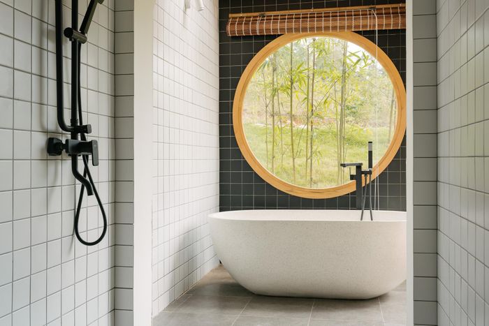 Toilet tầng 1 sử dụng bồn tắm chất liệu granite, tường và sàn được ốp gạch ngăn nắp. Để tối ưu ánh sáng trời, khu vực bồn tắm sử dụng rèm mành dân dã, kết hợp mái kính rào gỗ.