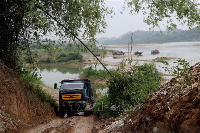 Các đối tượng khai thác cố ý đắp đường chặn dòng chảy cho các phương tiện cơ giới vận chuyển cát, sỏi. Ảnh: Vũ Quang - Nam Sương/TTXVN