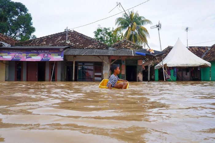 Cậu bé ngồi trong chiếc thùng nhựa để vượt qua dòng nước lũ do mưa lớn gây ra ở Serang, Indonesia, ngày 1/ 3. (Nguồn: Getty)