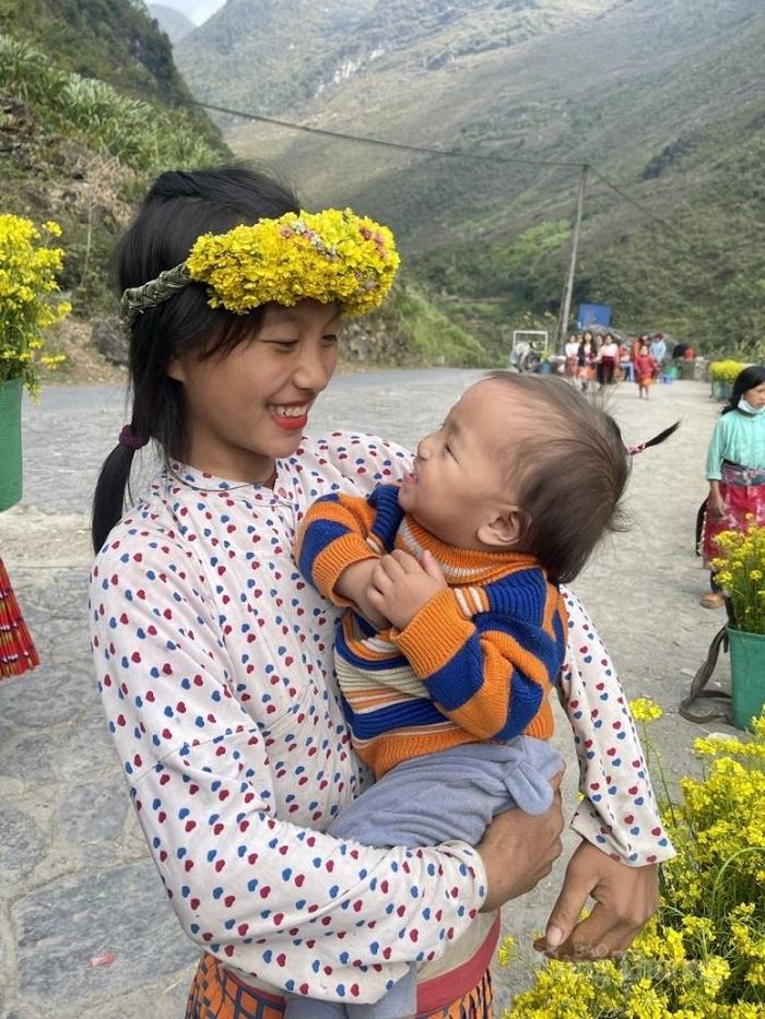 Người mẹ trẻ bồng theo con nhỏ đi bán đồ lưu niệm cho khách du lịch tại huyện Đồng Văn (Hà Giang)