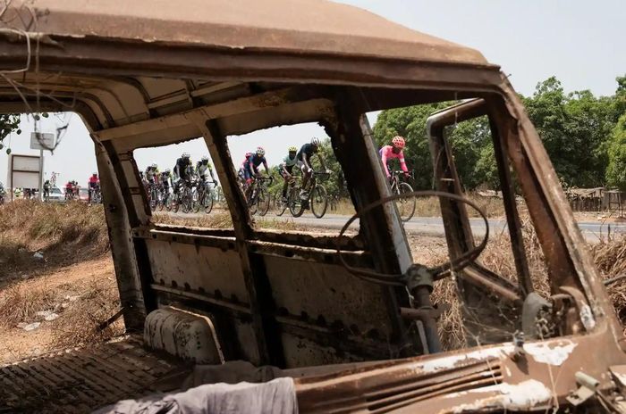 Những tay đua đi qua một chiếc ô tô bị cháy trên đường từ Freetown đến Lunsar. Ảnh: The Guardian.