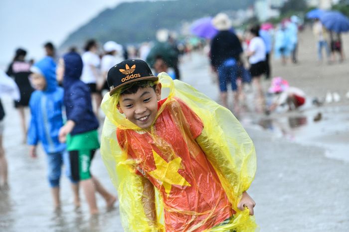 Dù vậy, nhiều du khách vẫn mặc áo mưa, che ô, mũ... để ra biển vui chơi khi trời còn đang mưa và gió lớn.