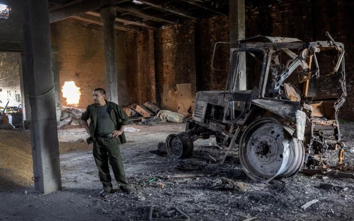 Một nông dân Ukraine đứng gần chiếc máy kéo bị đạn pháo phá hủy ở Cherkska Lozova, Ukraine. Ảnh: Getty Images