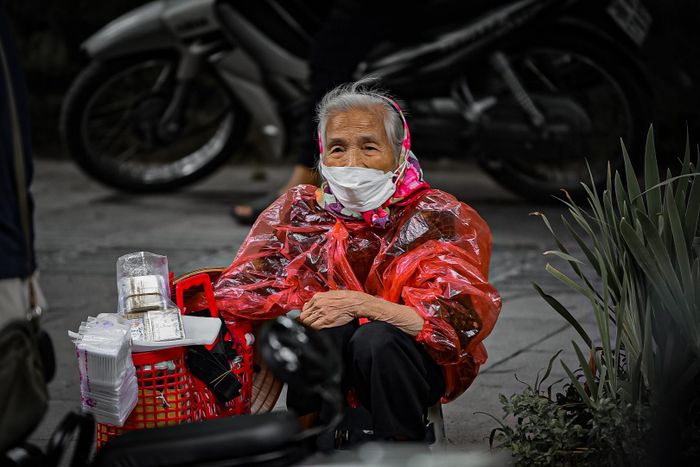 Bà cụ bán hàng rong lạnh co ro mặc thêm áo mưa cho đỡ lạnh.