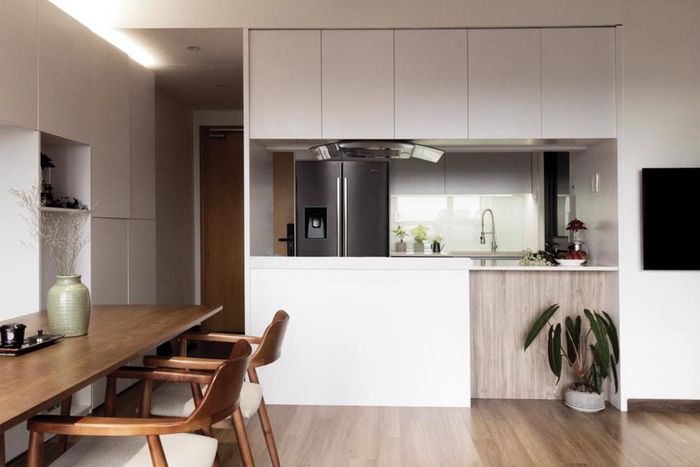 Để khắc phục hạn chế của không gian nhỏ, gian bếp có nhiều tủ chứa đồ, có bàn bar hướng ra bàn ăn, hệ tủ tích hợp ghế bàn ăn, sofa gắn tường và màu chủ đạo là trắng sữa để tạo cảm giác rộng thoáng.
