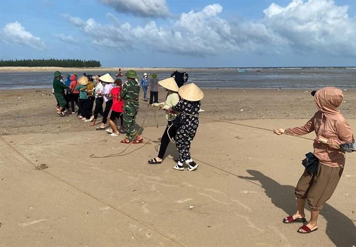 Cán bộ, chiến sĩ Đồn Biên phòng Roòn cùng nhân dân địa phương hỗ trợ kéo thuyền đánh cá của anh Phạm Thanh Huân vào bờ. Ảnh: Hoài Nam