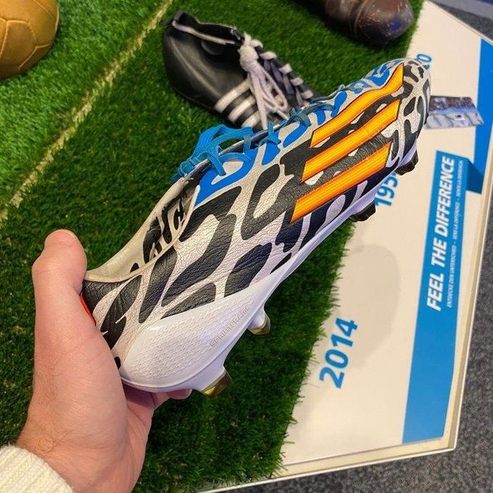 Tham gia giải đấu ở Brazil vào năm 2014, Messi sử dụng F50 adizero. Nó thuộc bộ sưu tập Battle Pack. Thiết kế chủ yếu mang màu đen - trắng có điểm nhấn là 3 vạch vàng đồng điệu với màu chiếc cúp chiến thắng. Các mẫu giày trong bộ sưu tập có hai màu trắng đen và logo vàng. Với đôi giày đá bóng của Messi, màu xanh ở phía trên liên quan đến áo đấu Argentina. Ảnh: FIFAmuseum. 