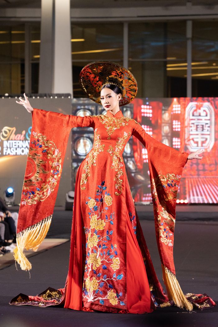 Hoa hậu Bảo Ngọc diện áo dài khăn đóng tông màu đỏ với họa tiết hoa được thêu tỉ mỉ, kỳ công dọc thân áo. Phần tay áo được cách điệu mang lại sự bay bổng và quyền lực cho người đẹp cao 1,85 m khi trình diễn trên sàn catwalk.