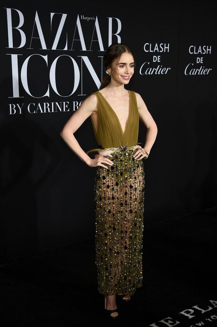 Lily Collins nổi bật với mẫu váy xẻ sâu màu xanh cho sự kiện Harper's Bazaar 2019. Chiếc váy do Georges Hobeika thiết kế bao gồm bộ bodysuit liền thân màu xanh, khoét sâu ở phần cổ. Phần chân váy là lớp trang sức trên vải sheer tạo ra hoa văn sọc trên váy, để lộ đôi chân thon dài của nữ diễn viên. Ảnh: Zimbio, Lily Collins News.