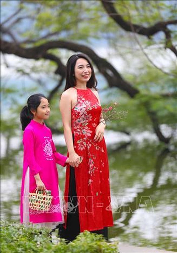 Du khách với tà áo dài thướt tha dạo Hồ Gươm trong tiết trời vào xuân.