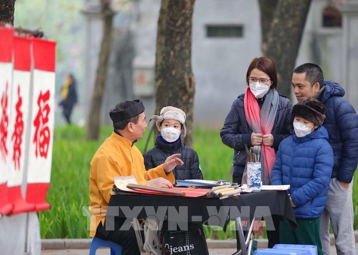 Một gia đình dừng chân bên ông đồ trước cửa đền Ngọc Sơn để nghe giải nghĩa về tục xin chữ đầu năm. Ảnh: Thanh Tùng - TTXVN