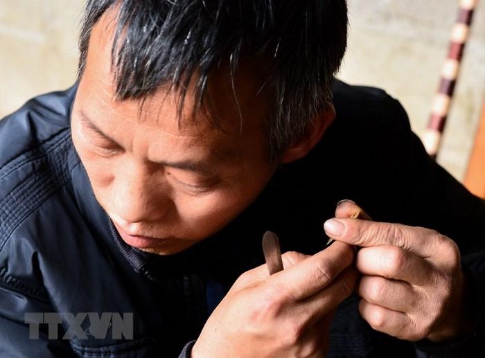  Nghệ nhân phải thẩm âm lá đồng trước khi gắn lên ống trúc. (Ảnh: Nam Thái/TTXVN)