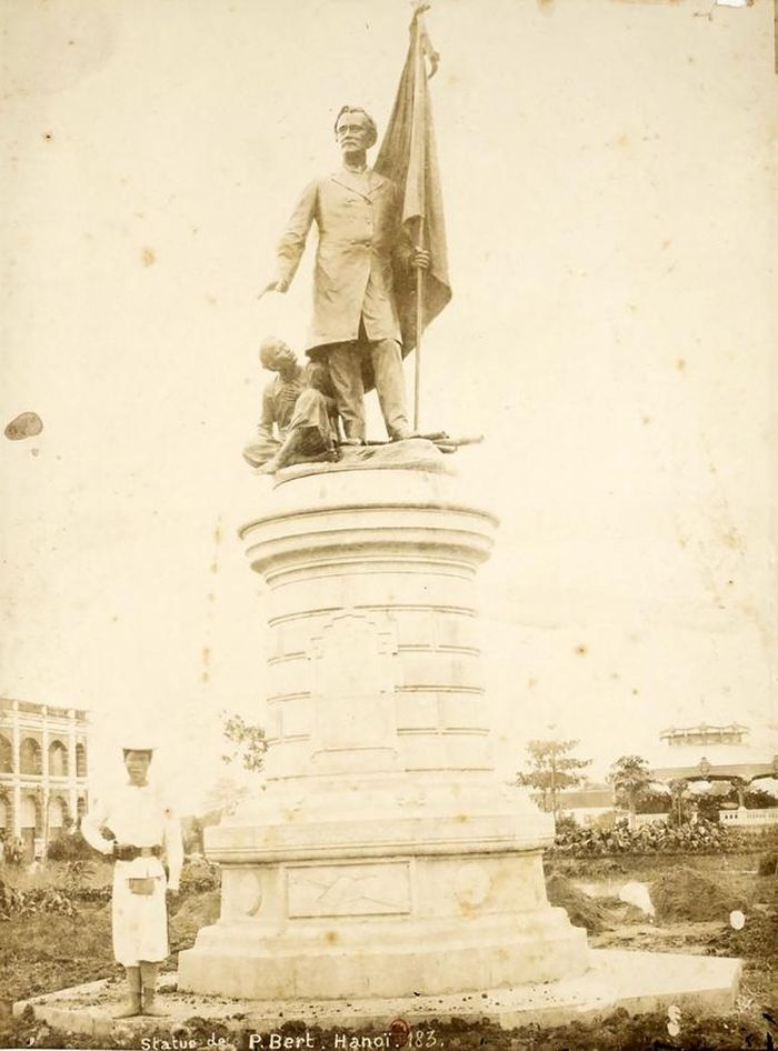 Paul Bert cầm lá cờ nước Pháp và một đứa bé bản xứ nép bên thể hiện vai trò bảo hộ của chính quốc