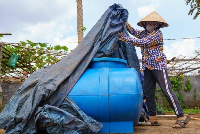  Sống chung với bụi, bà Thúy (người dân địa phương) dùng bạt bảo quản nước dự trữ, vật dụng tránh bụi tấn công. 