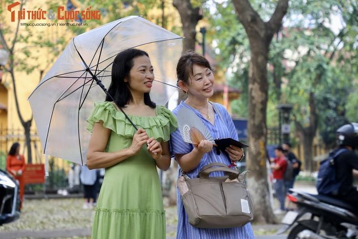 Một du khách Nhật Bản chụp ảnh kỉ niệm cùng người Việt trên con đường đẹp nhất Hà Nội phủ kín lá rụng.