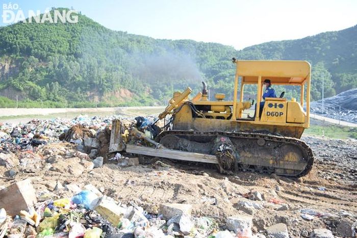 Xe ủi tiến hành san bằng đất, xà bần để phủ lên trên bề mặt rác nhằm giảm thiểu phân tán mùi hôi và làm đường cho xe vận chuyển rác tiếp tục di chuyển vào vùng đổ ở bên trong.