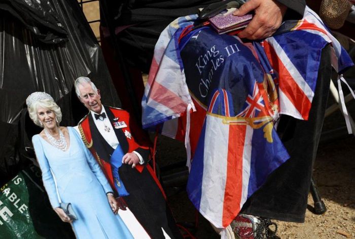 Một người phụ nữ ngồi cạnh tấm bìa cứng hình Vua Charles và Hoàng hậu Camilla của Anh. Rất nhiều đồ trang trí chào mừng lễ đăng quang được trưng bày xung quanh lều trại. (Ảnh: Reuters)