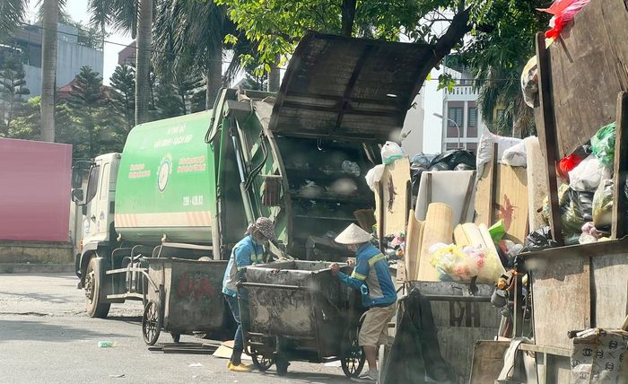 Công nhân môi trường thu gom rác lên xe ép rác tại phố Hoàng Trọng Mậu (quận Nam Từ Liêm). Ảnh: Dung Nhi
