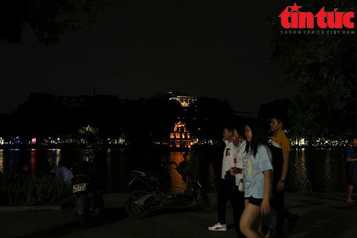 Những người đi dạo quanh hồ Gươm trong ánh sáng le lói.