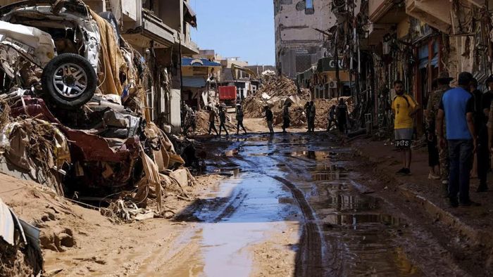 Người dân đi bên cạnh những ngôi nhà bị hư hại do lũ lụt ở Derna, Libya. Ảnh: CNN.