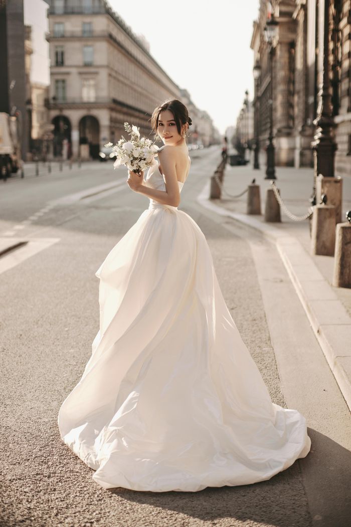 Chiếc váy cưới cúp ngực mang vẻ lộng lẫy và bồng bềnh trong mỗi bước đi. Cộng hưởng với màu trắng tinh khiết và phom dáng thay đổi linh hoạt, trước ngắn sau dài khiến khán giả dành không ít lời khen.