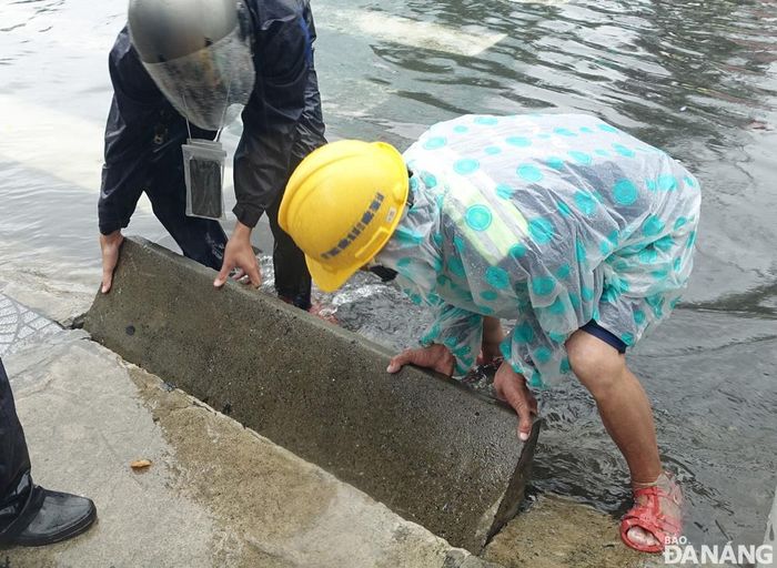 Công nhân của Công ty Thoát nước và xử lý nước thải Đà Nẵng phải tháo dỡ bó vỉa đường Hàm Nghi cho nước nhanh thoát xuống cống. Ảnh: HOÀNG HIỆP