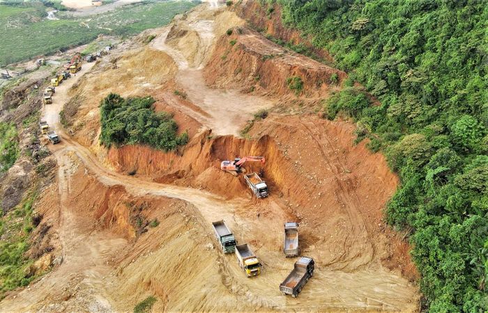 Máy xúc hoạt động hết công suất để xúc đất đưa lên nhiều xe tải nối đuôi nhau chờ sẵn.