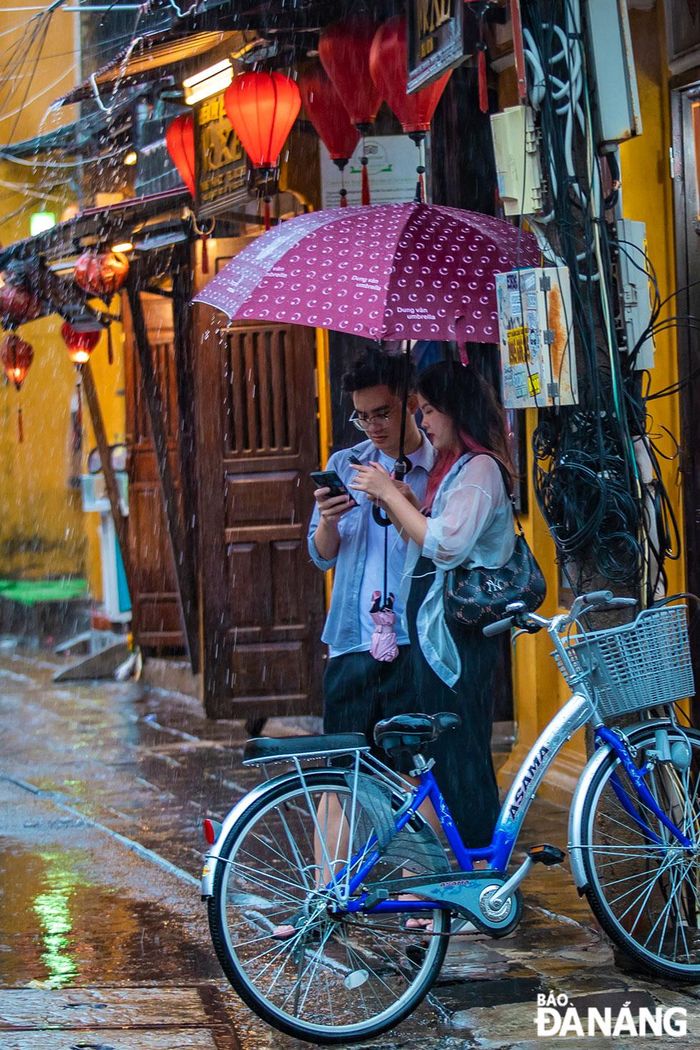 Đôi bạn đứng bên mái hiên chờ cơn mưa ngớt hạt.