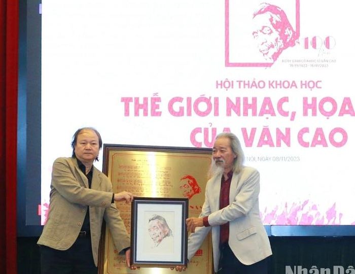 Họa sĩ Nghiêm Thành (trái) và nhạc sĩ Văn Thao, đại diện gia đình nhạc sĩ Văn Cao nhận tranh tặng từ Ban tổ chức
