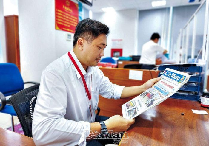 Anh Lê Hoàng Anh, công chức Sở Tài chính tỉnh Cà Mau tranh thủ đọc báo khi chưa có khách hàng đến giao dịch.