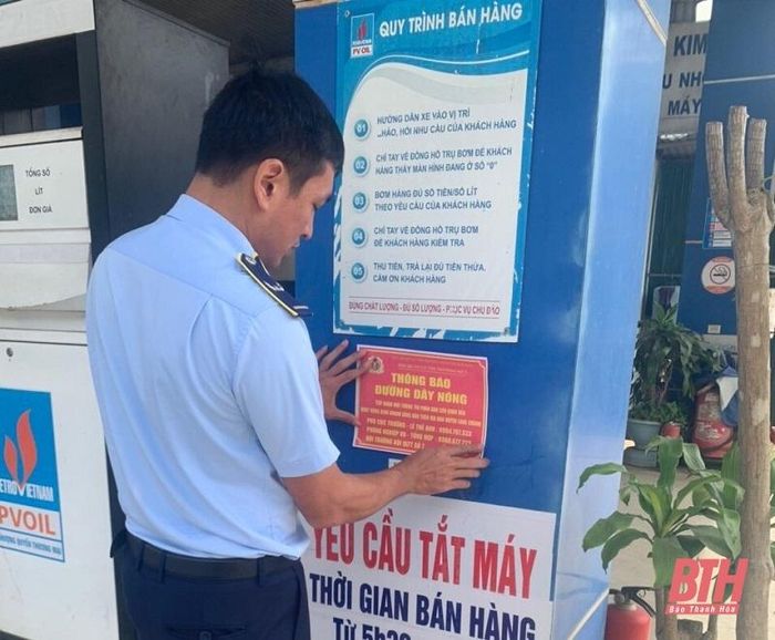 Cán bộ Đội Quản lý thị trường số 7 dán thông báo số điện thoại đường dây nóng tại các cửa hàng bán lẻ xăng dầu để tiếp nhận các thông tin, phản ánh của người dân .