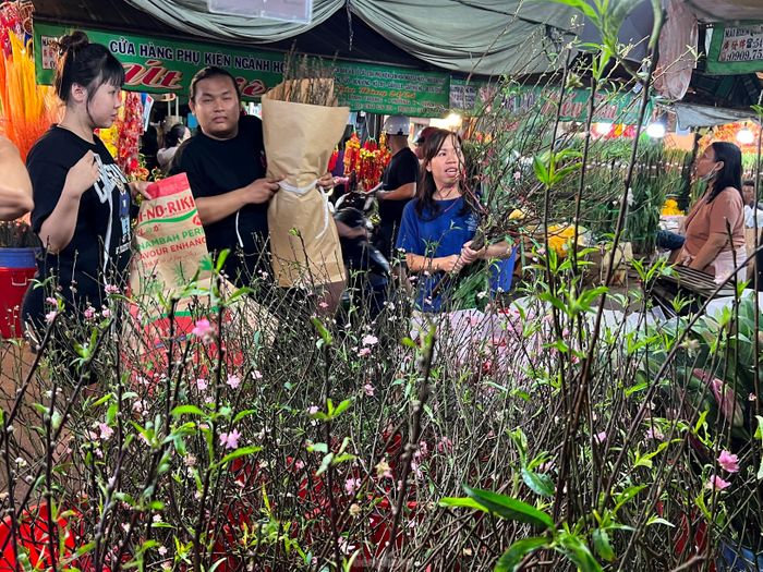Anh Nguyễn Huy Hoàng Nam (giữa), sạp Vân Nhuận giới thiệu các loại đào phai cho khách với giá chỉ 200.000 đồng/cành. Anh Nam cho biết, anh có vườn đào ở Hà Nội nên luôn có cây đẹp và giá mềm nhất so với nhiều quầy hàng khác. "Vài ngày gần đây khách mua có tăng lên nhưng vẫn thua với giai đoạn 2 năm trước. Lúc ấy đào cành chất đầy ki-ốt, khách đi bộ phải nhích từng chút một" - anh Nam nói.