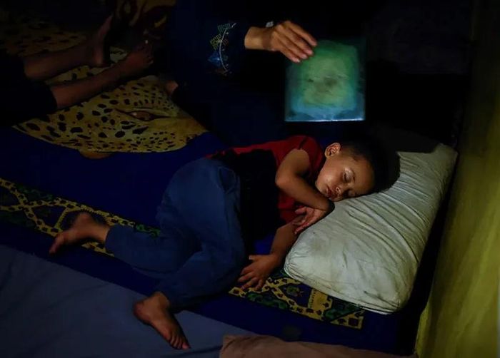Một bà mẹ quạt cho con ngủ trong thời tiết nóng bức và mất điện. Để mua thực phẩm, hơn một nửa số hộ gia đình Palestine được khảo sát phải bán quần áo và 1/3 phải nhặt rác để bán.