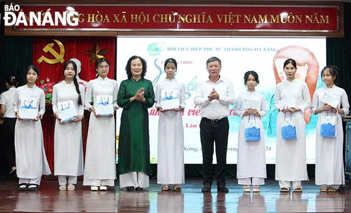 Chủ tịch Ủy ban MTTQ Việt Nam thành phố Lê Văn Trung (thứ 4, bên phải sang) trao áo dài và quà cho nữ sinh vượt khó. Ảnh: X.D