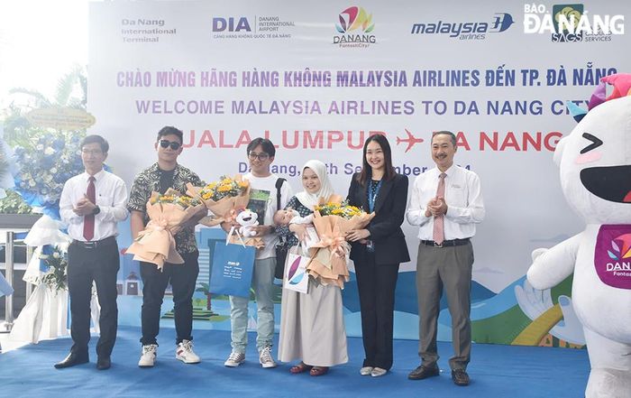 Đại diện ngành du lịch thành phố và hãng hàng không tặng quà chúc mừng những hành khách may mắn trên chuyến bay đầu tiên của Malaysia Airline. Ảnh: THU HÀ
