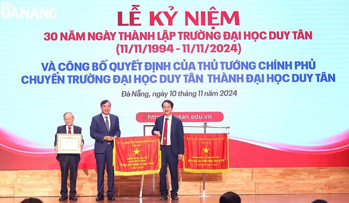 Chủ tịch UBND thành phố Đà Nẵng Lê Trung Chinh (giữa) trao bằng khen của Ban Thường vụ Thành ủy và tặng cờ ghi nhận thành tích cho Đại học Duy Tân. Ảnh: THU HÀ
