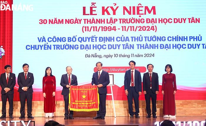 Bộ trưởng Bộ Giáo dục và Đào tạo Nguyễn Kim Sơn (thứ 5 từ trái sang), thừa ủy quyền của Thủ tướng Chính phủ lên trao cờ thi đua cho tập thể lãnh đạo Đại học Duy Tân. Ảnh: THU HÀ