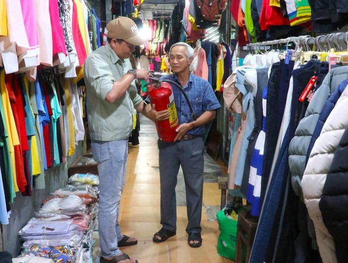  Ông Lâm Kim Trụ (bên phải)-chủ gian hàng kinh doanh quần áo tại chợ An Khê trao đổi cách sử dụng bình chữa cháy với lực lượng chữa cháy cơ sở. Ảnh: Ngọc Minh 