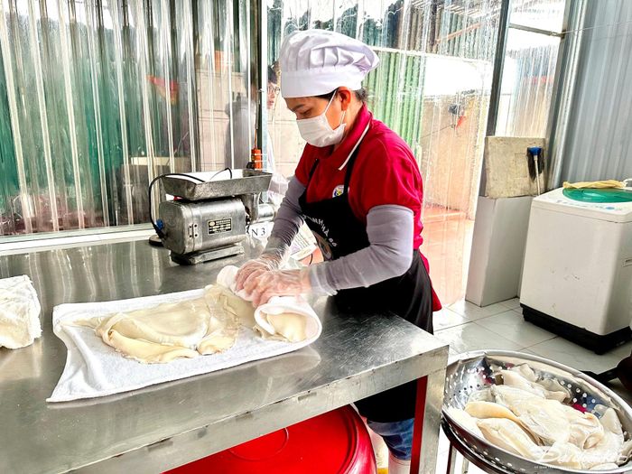 Sau khi rửa sạch, công nhân chế biến dùng khăn sạch thấm, lau, vắt khô con mực trước khi cho vào xay, giã.