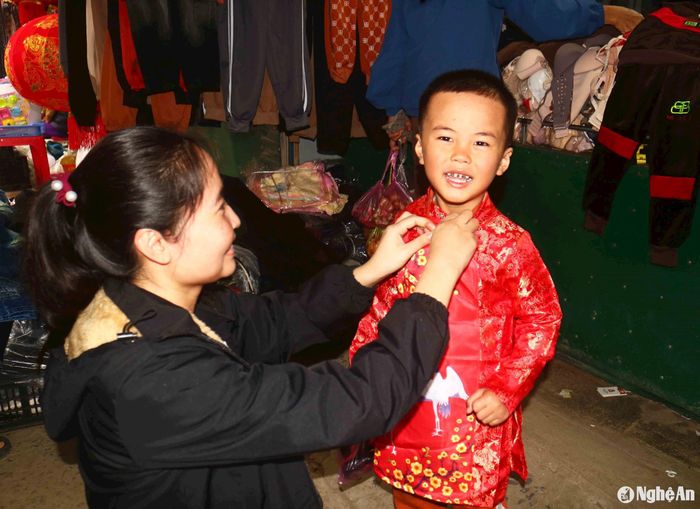 Những chiếc áo dài đỏ được bố mẹ chọn mua cho con trẻ mặc trong dịp Tết. Một em nhỏ thích thú khi mặc thử áo dài giữa chợ Cồn xã Xuân Dương (Thanh Chương). Ảnh: Huy Thư