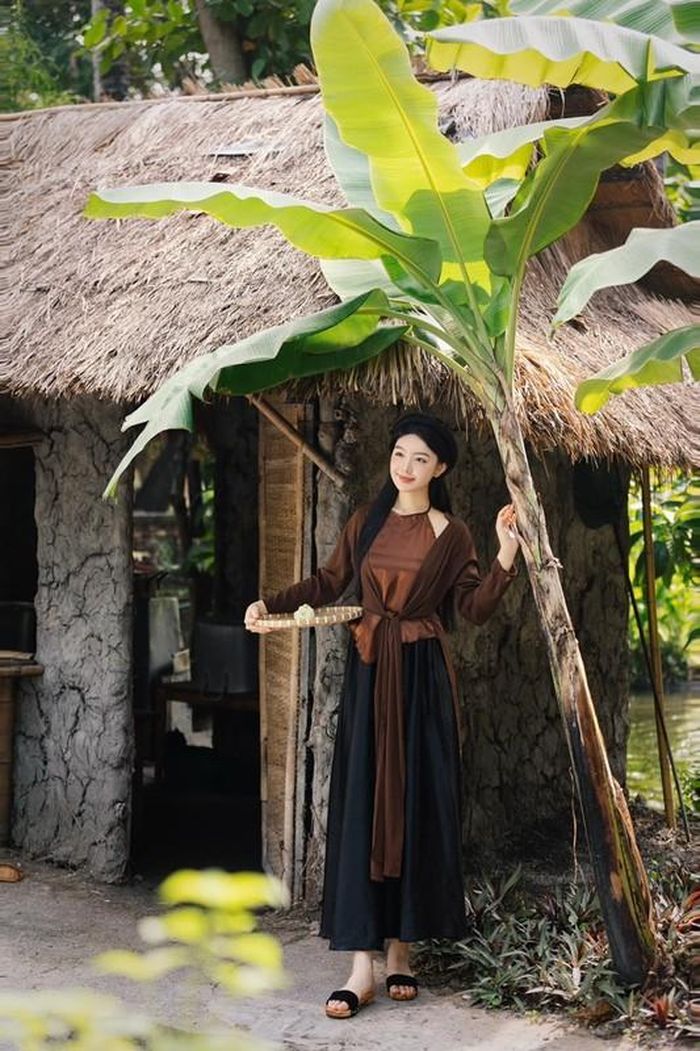 Lọ Lem chọn áo tứ thân màu nâu trầm kết hợp yếm đào, tóc buông xõa tự nhiên, trang điểm nhẹ nhàng phù hợp với không gian làng quê yên bình.