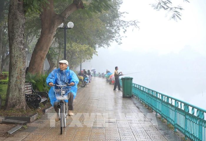 Người dân phải áo mưa vì trời xuất hiện mưa phùn, mưa nhỏ ở khu vực đường Thanh Niên và Hồ Tây. Ảnh: Nguyễn Hoa/TTXVN phát